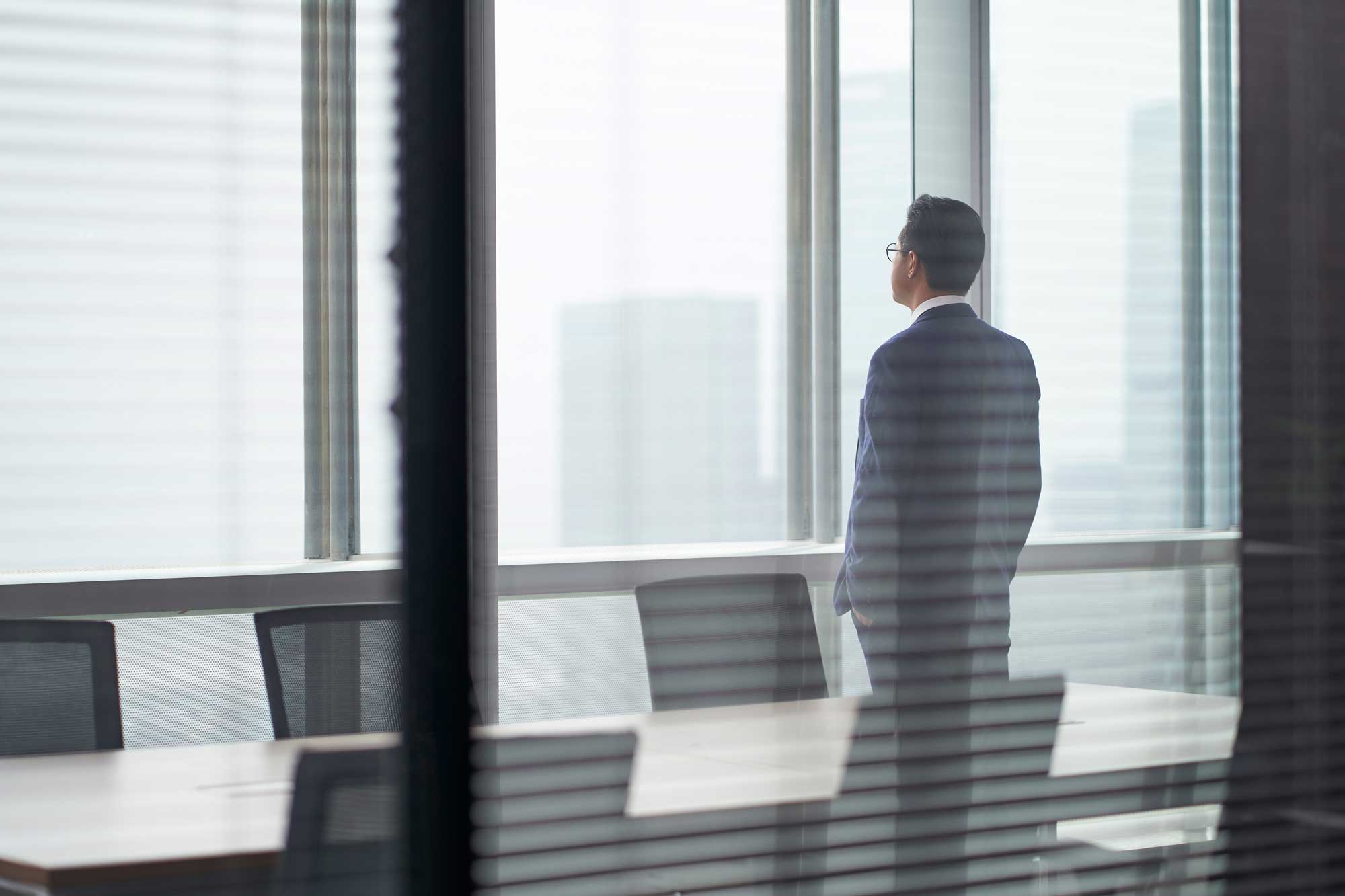 asian-corporate-executive-standing-in-front-of-window-thinking